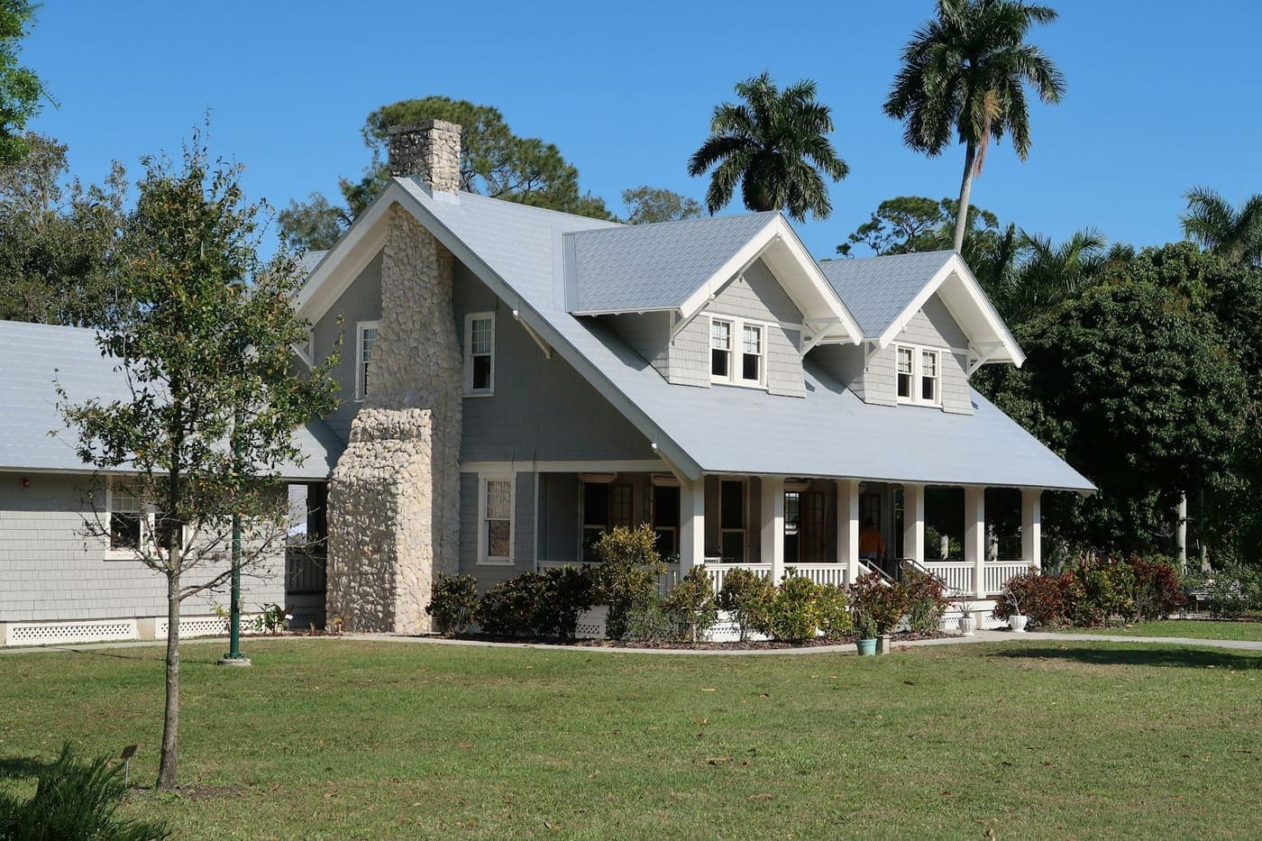 Gray craftsman with a stone chimney and wraparound porch